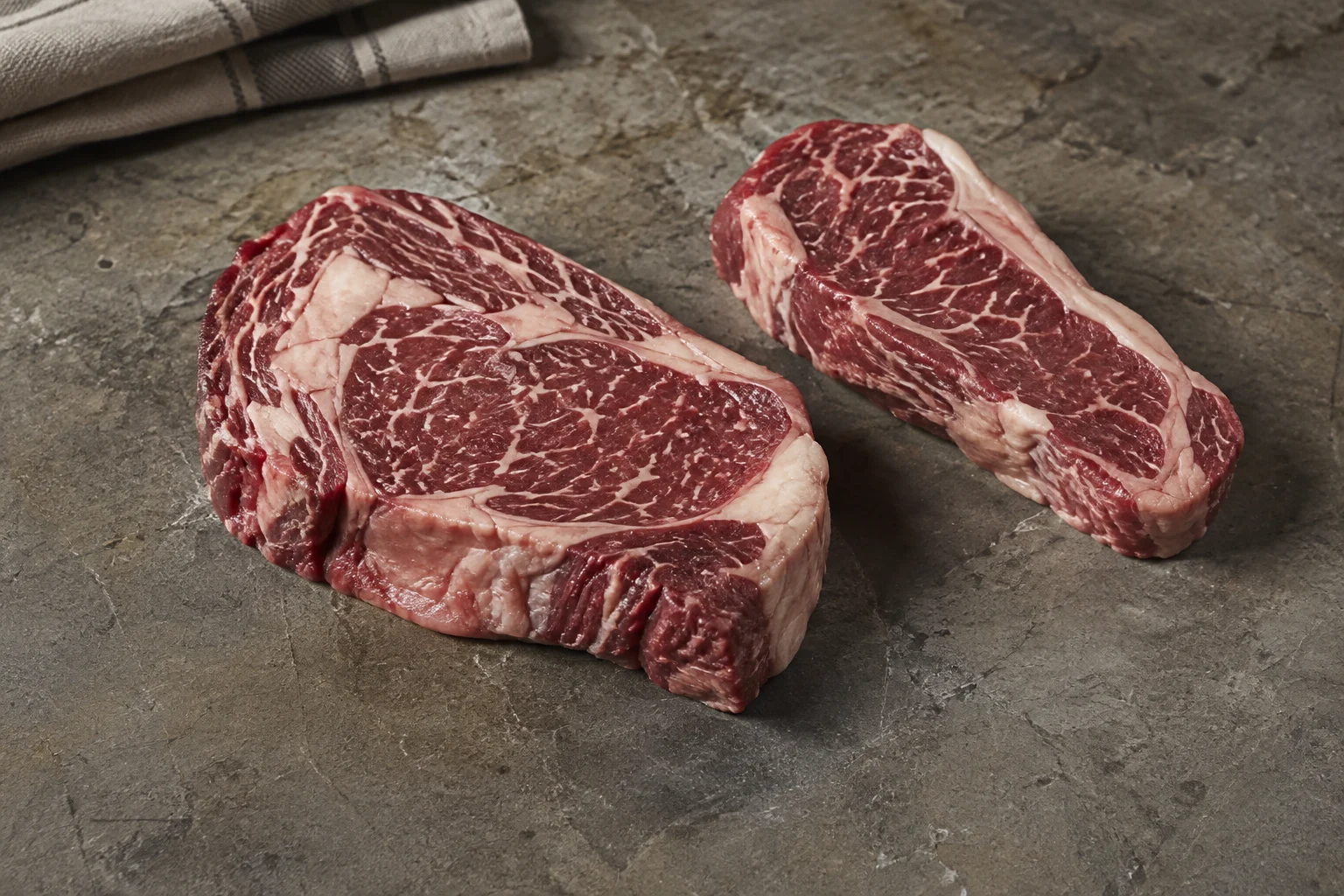 Rib-Eye und Striploin auf einer Steinfläche